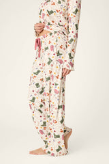 A person standing barefoot on a neutral background is shown from the lower body and midsection, wearing P.J. Salvage Saddle Up Western Print Pajama Pants featuring a colorful floral and animal pattern.