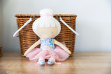 Baby ballerina doll in a fluffy tulle tutu and floral bodice, seated with a wicker basket in the background.
