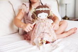 40cm Fleur Fairy doll in blush gold dress with floral crown, held by child on bed.